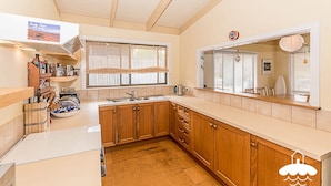 A compact kitchen with wooden cabinets, a sink, and a window with blinds.