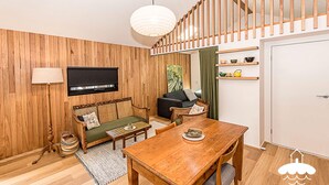 A cozy living room with a wooden floor, a sofa, a dining table, and a TV mounted on the wall.