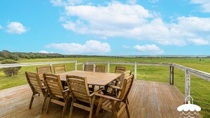 Une terrasse en bois avec une table et des chaises donnant sur un champ verdoyant où paissent des vaches.