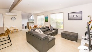 Un salon moderne avec un canapé gris, un pouf assorti et un coin repas comprenant une table et des chaises.
