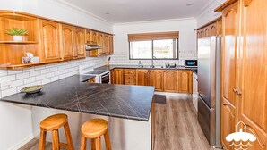 A modern kitchen with wooden cabinets, a black marble countertop, and two wooden stools. - Fishermans Stay at Port Franklin (Port Franklin)