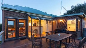A wooden deck with a dining table and chairs, a kitchen area with a dining table, and a covered outdoor seating area.