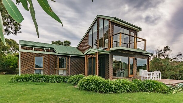 A modern two-story house with large windows and a green roof, surrounded by well-maintained lawns and shrubs.
