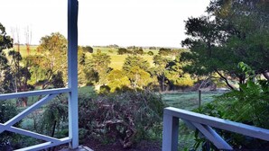 Une vue depuis un balcon doté d’une balustrade, donnant sur un champ verdoyant avec des arbres et un bâtiment situé au loin.