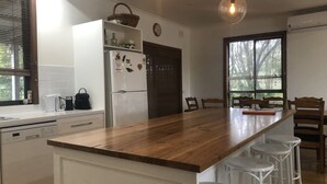 Une cuisine avec un plan de travail en bois, des meubles blancs, un réfrigérateur et une fenêtre avec des stores.