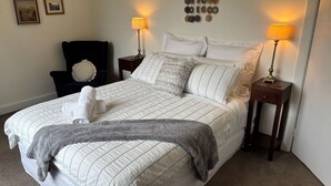 Un lit bien fait, avec une couette blanche et des oreillers, deux lampes de chevet, une chaise et un mur orné d’objets décoratifs.
