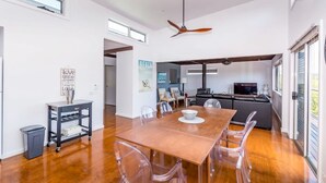 A spacious dining area with a wooden table and clear chairs, a black sofa, and a television in the background.