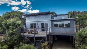 A modern two-story house with a deck, large windows, and a covered outdoor area.