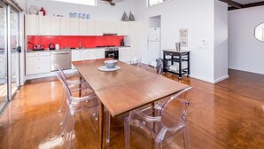 A modern kitchen with white cabinets, a red backsplash, and a wooden dining table with clear chairs.