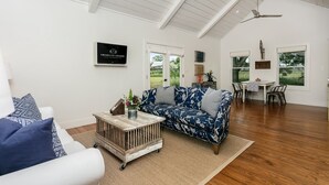 A spacious living room with a high ceiling, a blue floral sofa, a white armchair, and a rustic coffee table. - Smith House | 2/1, Kitchenette, Gas Firepit (Fredericksburg)