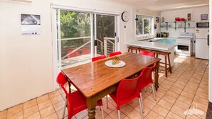 Un coin repas avec une table en bois et des chaises rouges, une cuisine avec des appareils électroménagers blancs, et une porte-fenêtre coulissante donnant sur un balcon.