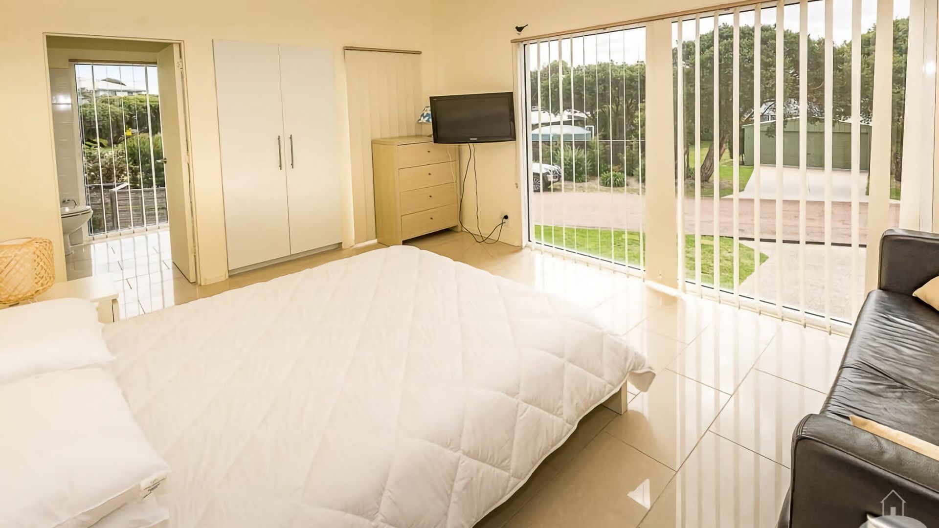 Ein Schlafzimmer mit Bett, Fernseher, Kleiderschrank und einem Balkon mit Blick ins Freie.