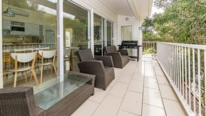 A balcony with wicker furniture, a glass table, and a grill.