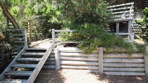 Un escalier en bois mène à une terrasse en bois, elle-même entourée de verdure.