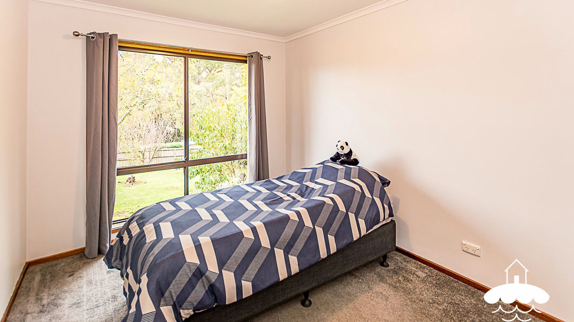 A bedroom with a bed, a window with curtains, and a view of greenery outside.