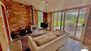 A cozy living room with a brick wall, a fireplace, a television, and a sliding glass door leading to an outdoor patio.