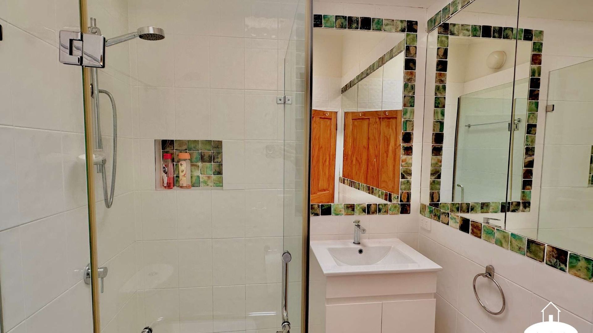 Une salle de bain avec une douche à parois de verre, un lavabo et un miroir orné de motifs en mosaïque.
