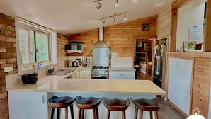 A modern kitchen with a central island, wooden walls, a microwave, stove, and a refrigerator.