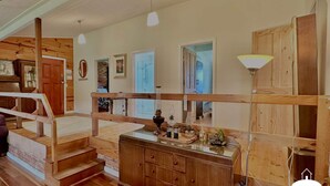 A rustic cabin interior with a wooden staircase, a wooden dresser, and a mirror.