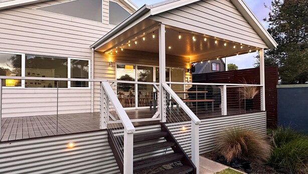 A modern house with a covered porch, a staircase, and a barbecue area.