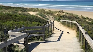 A wooden boardwalk leading to a beach with a sandy path and a wooden fence.