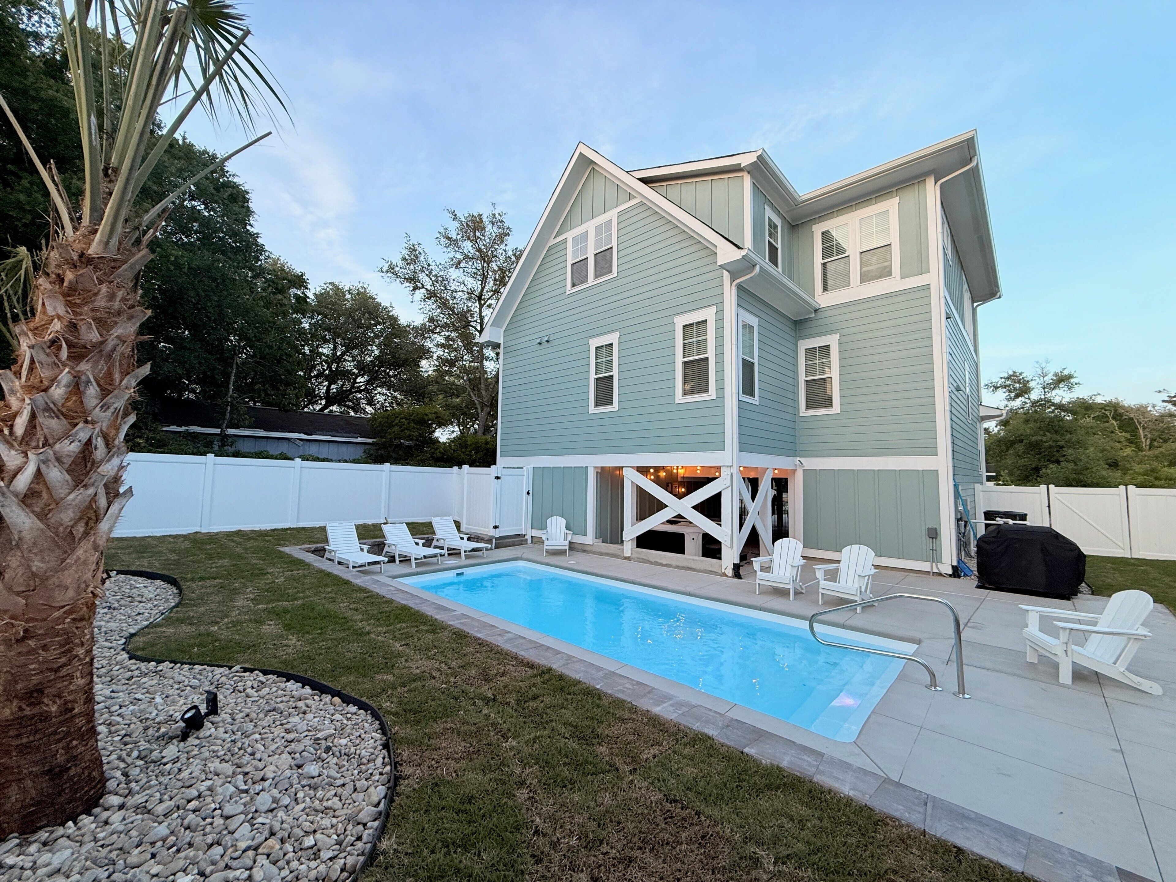 A two-story house with a swimming pool, white deck chairs, and a covered patio area.