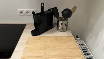A kitchen counter with a black coffee maker, a wooden cutting board, a stainless steel utensil holder, and a vent.