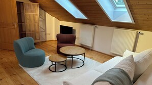 A cozy attic room with a sloped ceiling, wooden flooring, a sofa, a round table, and a chair. - Modern apartment in the countryside (Niedertaufkirchen)