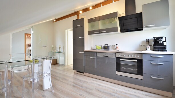 A modern kitchen with a glass dining table, stainless steel appliances, and a minimalist design. - Modern apartment in the countryside (Niedertaufkirchen)