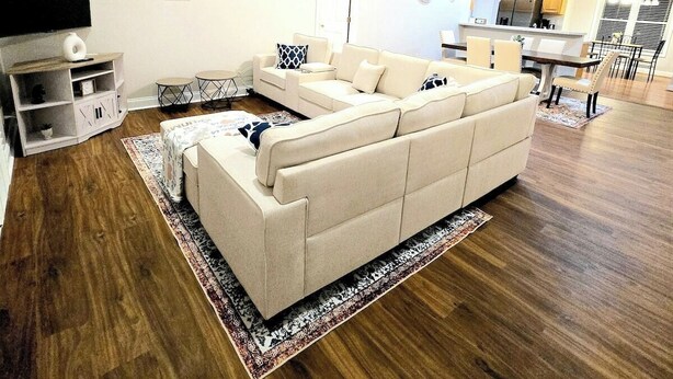 Una sala moderna con un sofá seccional, piso de madera, un televisor de pantalla plana y una zona de comedor con cocina al fondo.