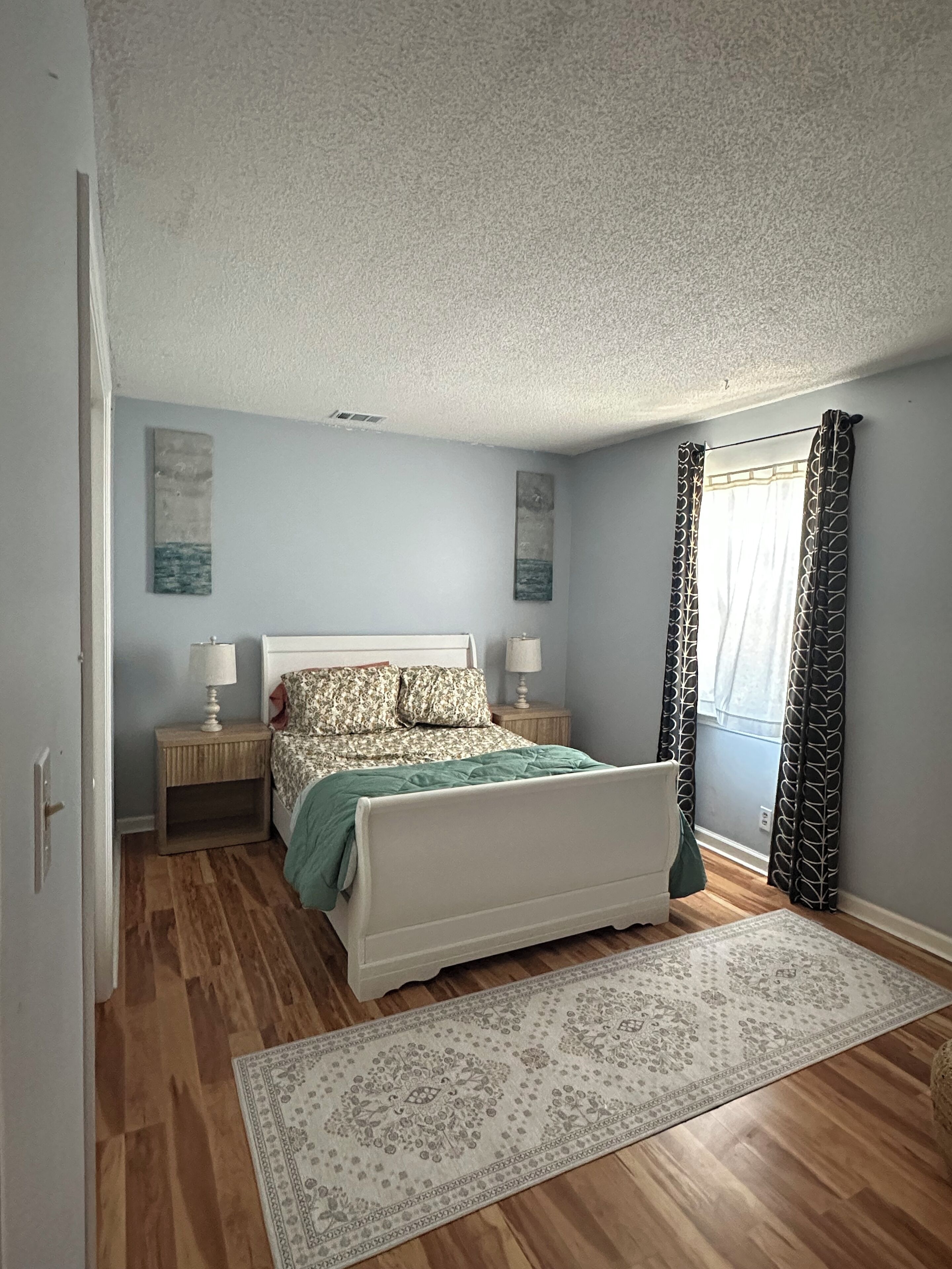 A bedroom with a bed, nightstands, a rug, and a window with curtains.