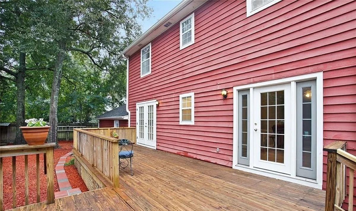 A red wooden house with a deck, white doors, and windows.