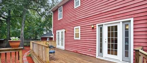 A red wooden house with a deck, white doors, and windows.
