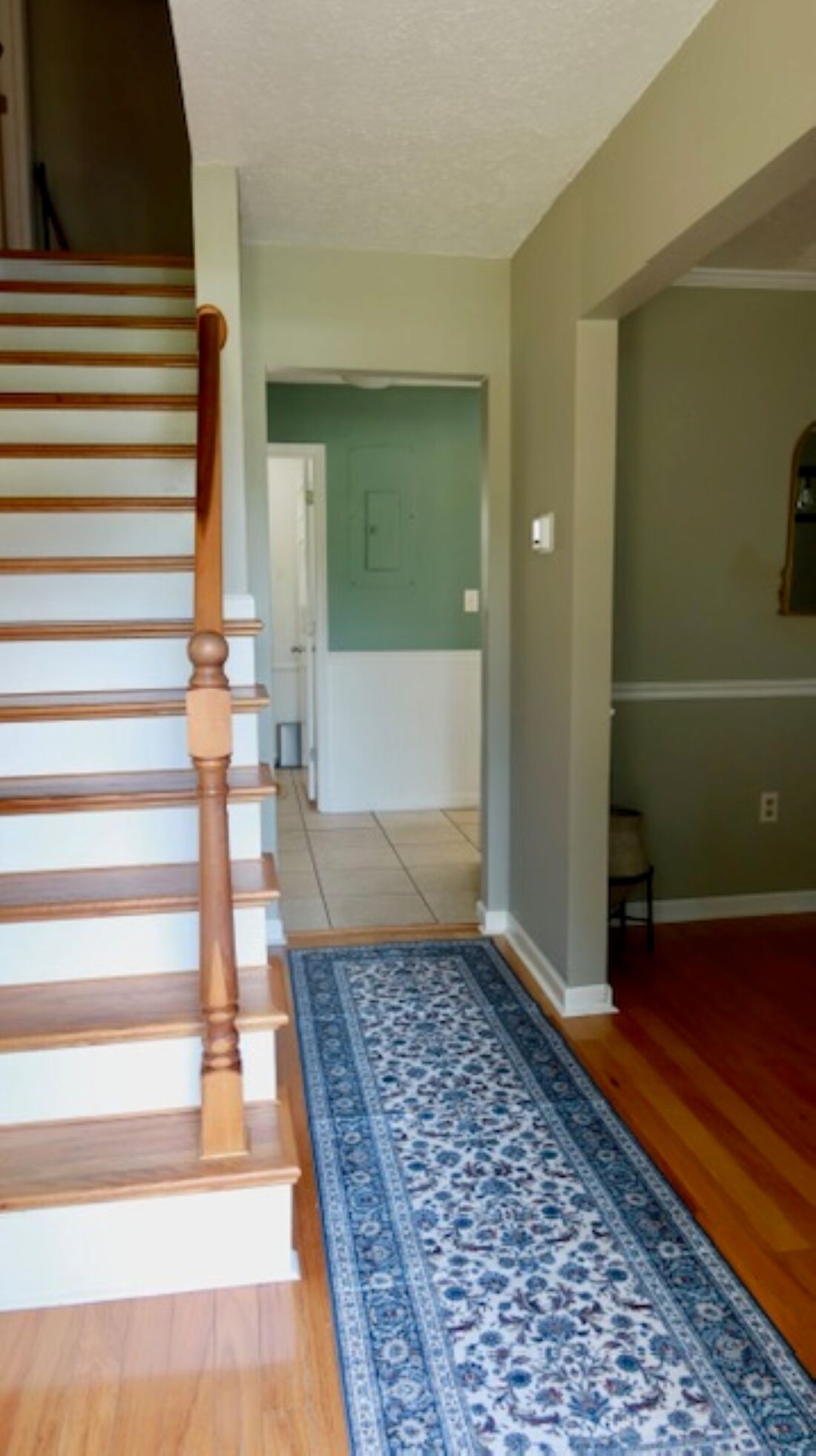 Una escalera con barandillas de madera que lleva a una plataforma. Un tapete azul con estampado está en el suelo.