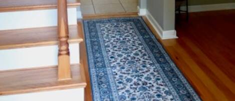 Una escalera con barandillas de madera que lleva a una plataforma. Un tapete azul con estampado está en el suelo.