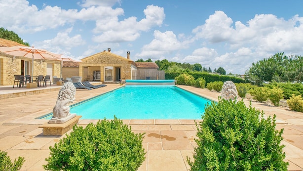 A swimming pool with stone tiles, a stone statue, and a building with a tiled roof. - Charmante Maison avec piscine (La Douze)