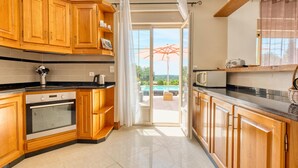 A kitchen with wooden cabinets, a black countertop, and a view of a pool through an open door. - Charmante Maison avec piscine (La Douze)
