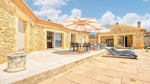 A stone building with a patio area featuring outdoor furniture and umbrellas. - Charmante Maison avec piscine (La Douze)