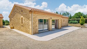 A stone building with a tiled roof, large glass doors, and a gravel driveway. - Charmante Maison avec piscine (La Douze)