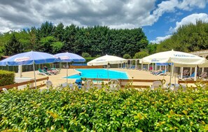 A pool area with lounge chairs and umbrellas, surrounded by greenery.