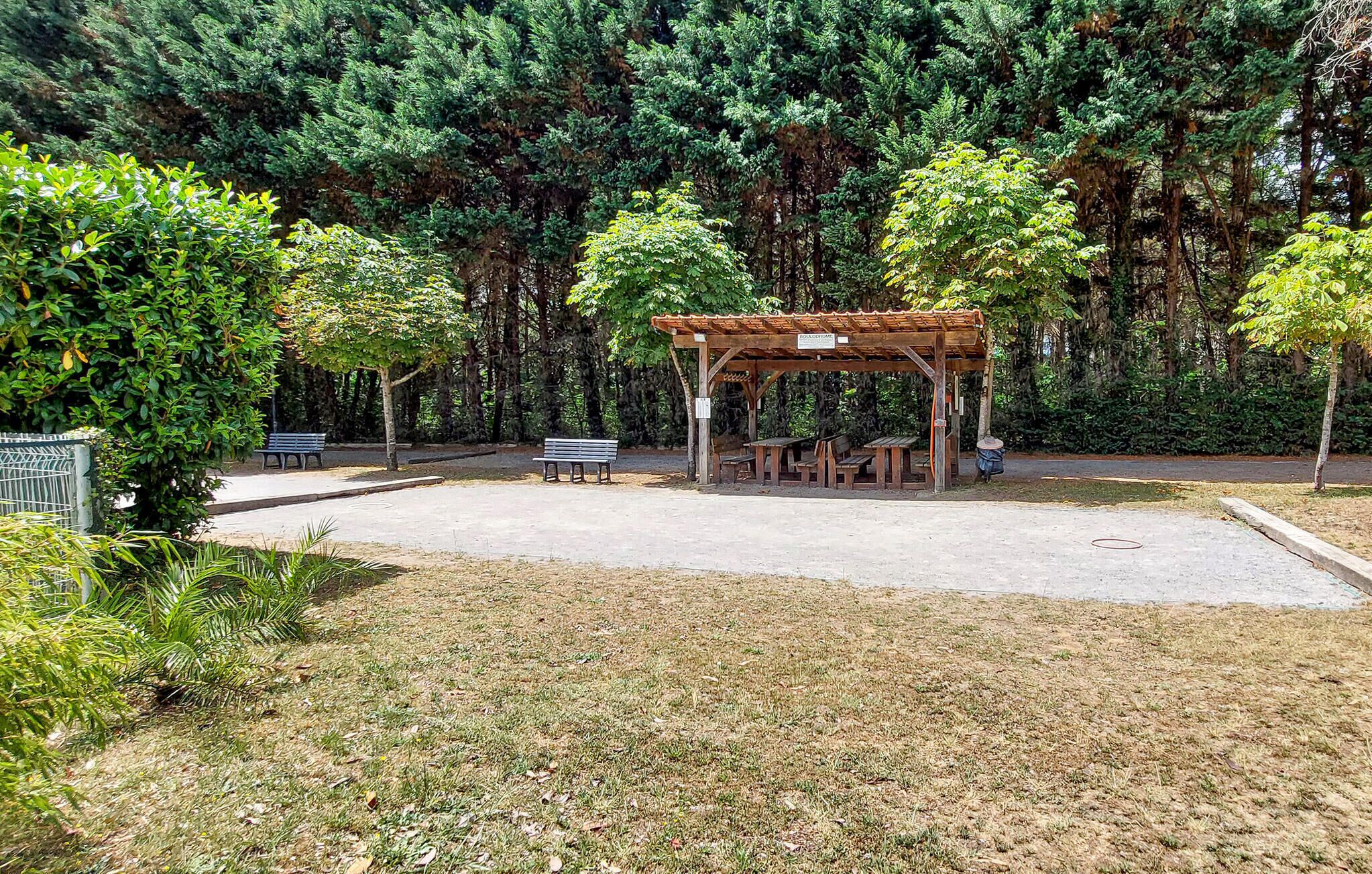 A park with a wooden gazebo, picnic tables, benches, and a paved area.
