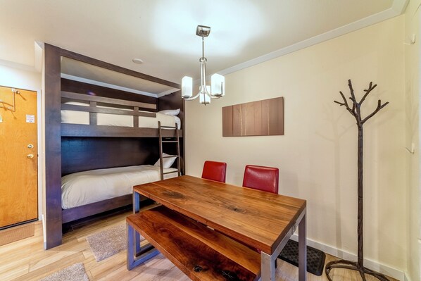 A compact room with a bunk bed, a wooden table, red chairs, and a coat rack.