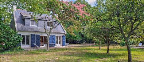 A two-story house with a sloped roof, blue shutters, and a front porch with outdoor seating.