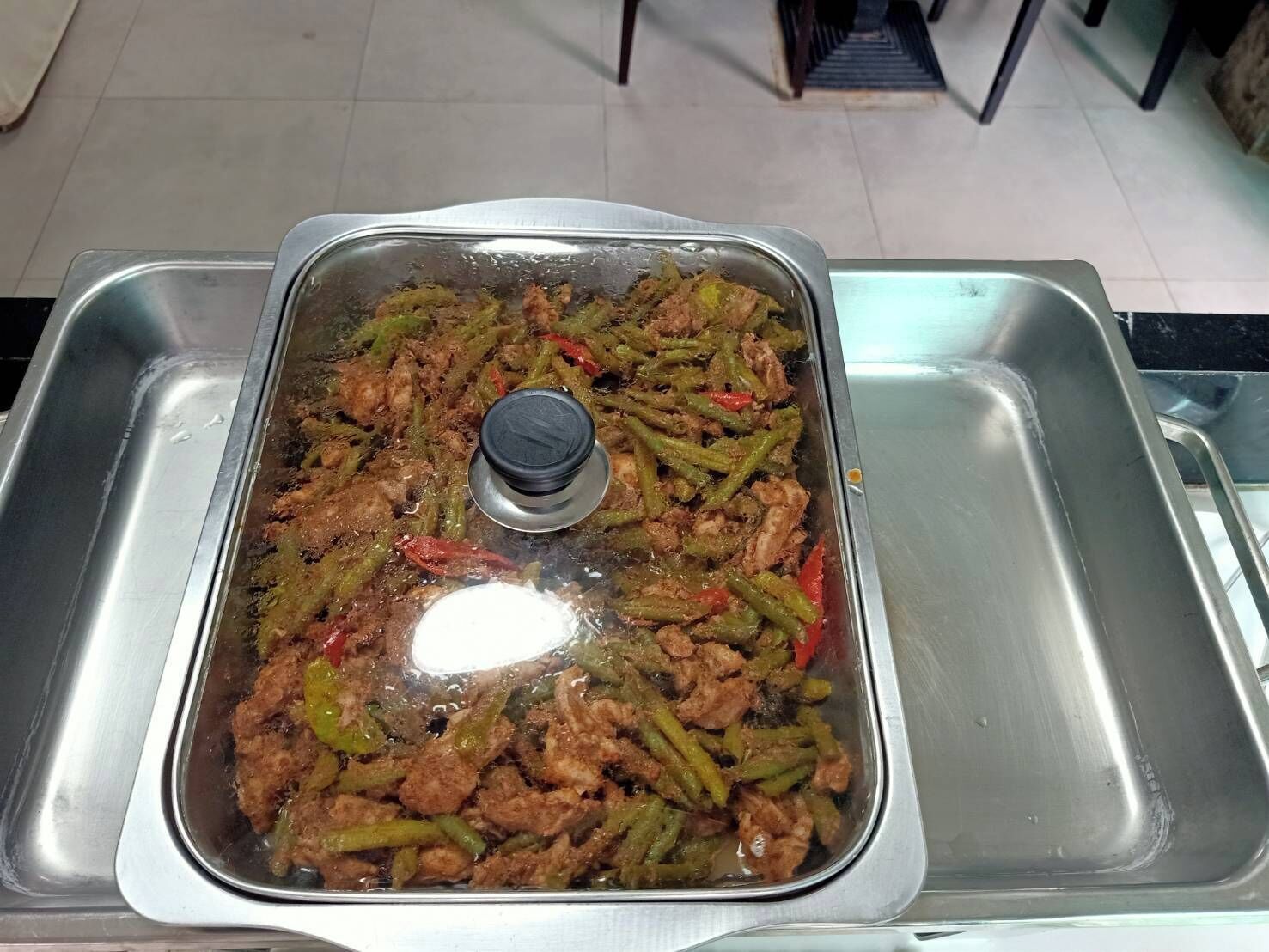 A stainless steel buffet sink with a covered dish of stir-fried meat and vegetables.