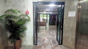 A hallway with a potted plant, marble flooring, and an emergency exit sign. - Mapeak Hotel (Chiang Mai)