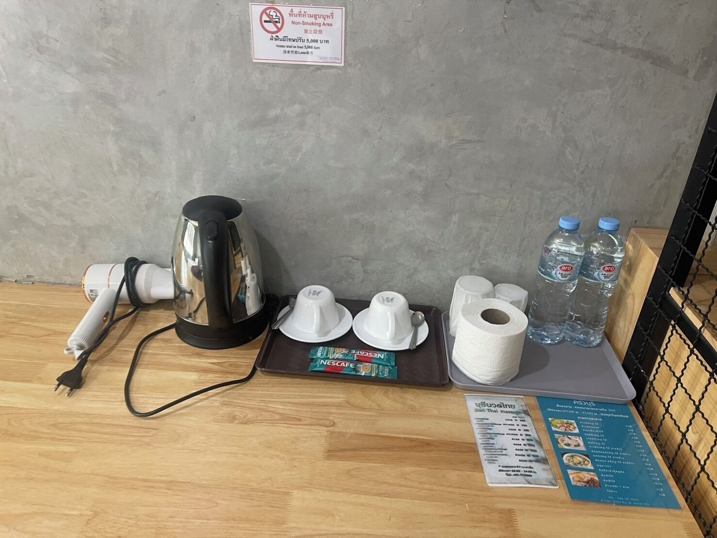 A hotel room with a coffee maker, water bottles, a Nescafe coffee pod, a roll of toilet paper, and a menu on the table.