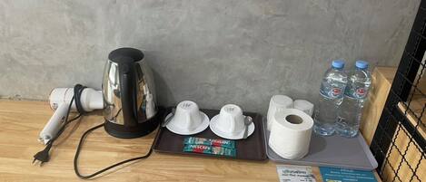 A hotel room with a coffee maker, water bottles, a Nescafe coffee pod, a roll of toilet paper, and a menu on the table.