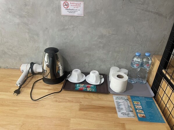 A hotel room with a coffee maker, water bottles, a Nescafe coffee pod, a roll of toilet paper, and a menu on the table. - Mapeak Hotel (Chiang Mai)