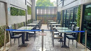 A restaurant with tables and chairs arranged outdoors, a blue rope barrier, and a sign indicating a reservation time. - Mapeak Hotel (Chiang Mai)