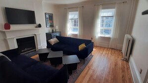 A living room with a fireplace, two sofas, a coffee table, and a flat-screen TV mounted above the fireplace.